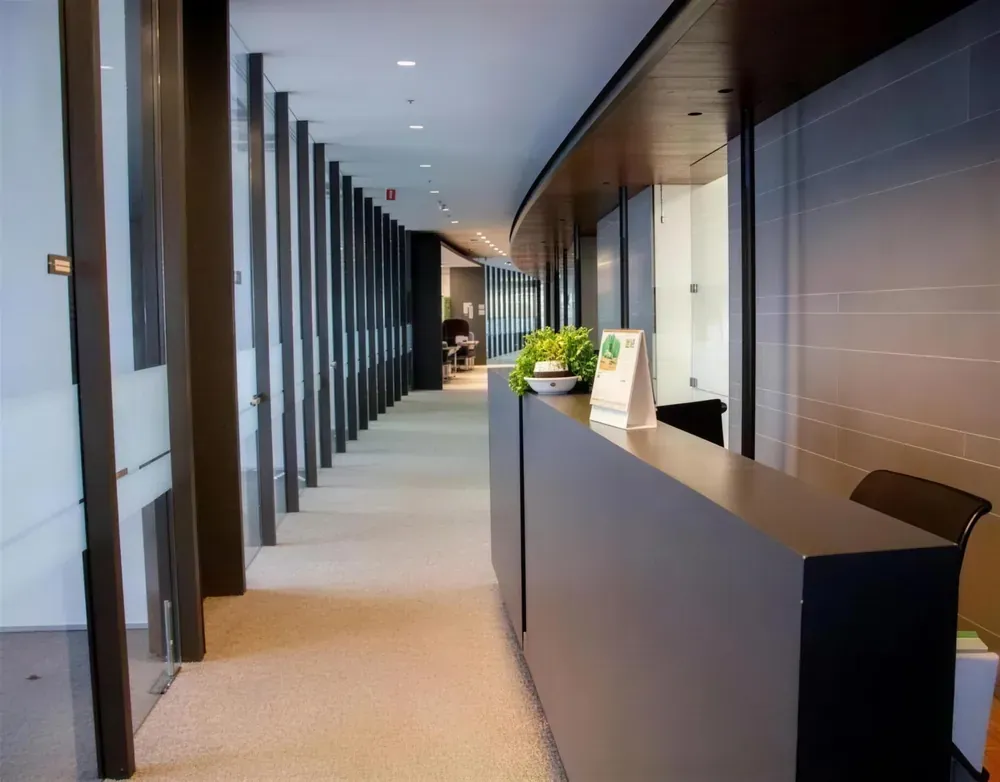 Pasillo de oficinas con mostrador oscuro, columnas y cristal, piso alfombrado