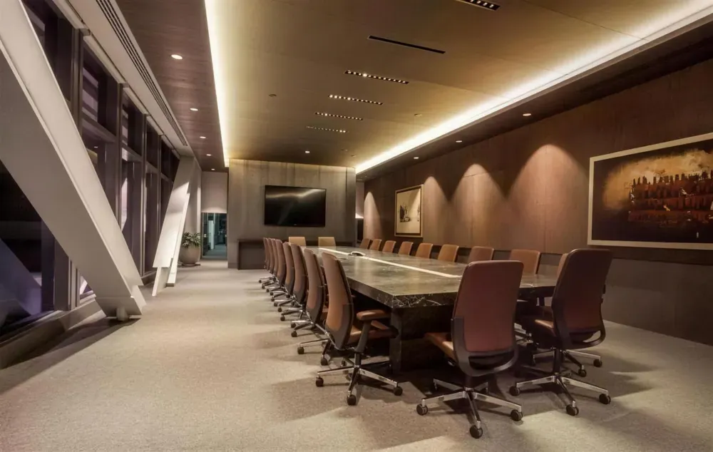 Sala de consejo con mesa larga en piedra, sillas de piel y plafón con iluminación indirecta