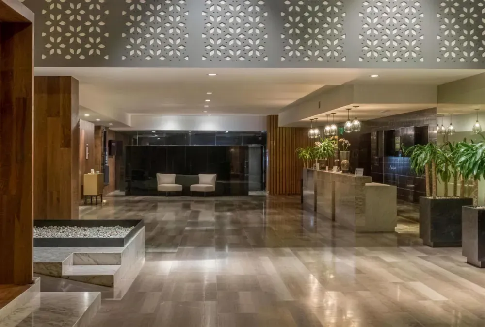Área pública de hotel con celosía calada, piso de piedra, jardinera y mostrador de recepción