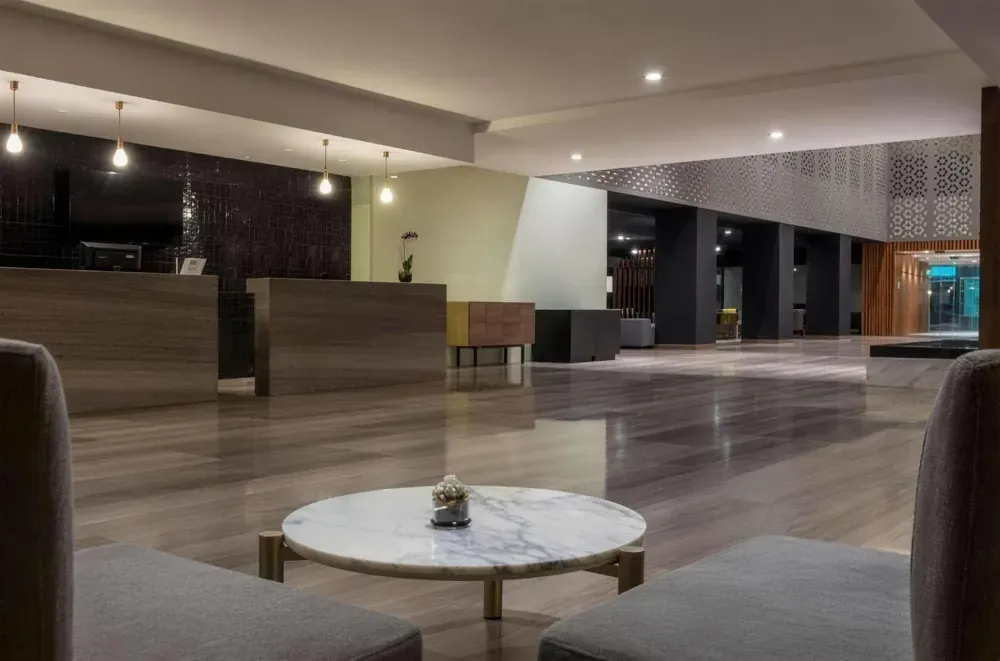 Lobby de hotel con recepción en piedra, piso de gran formato y mesa de centro en mármol