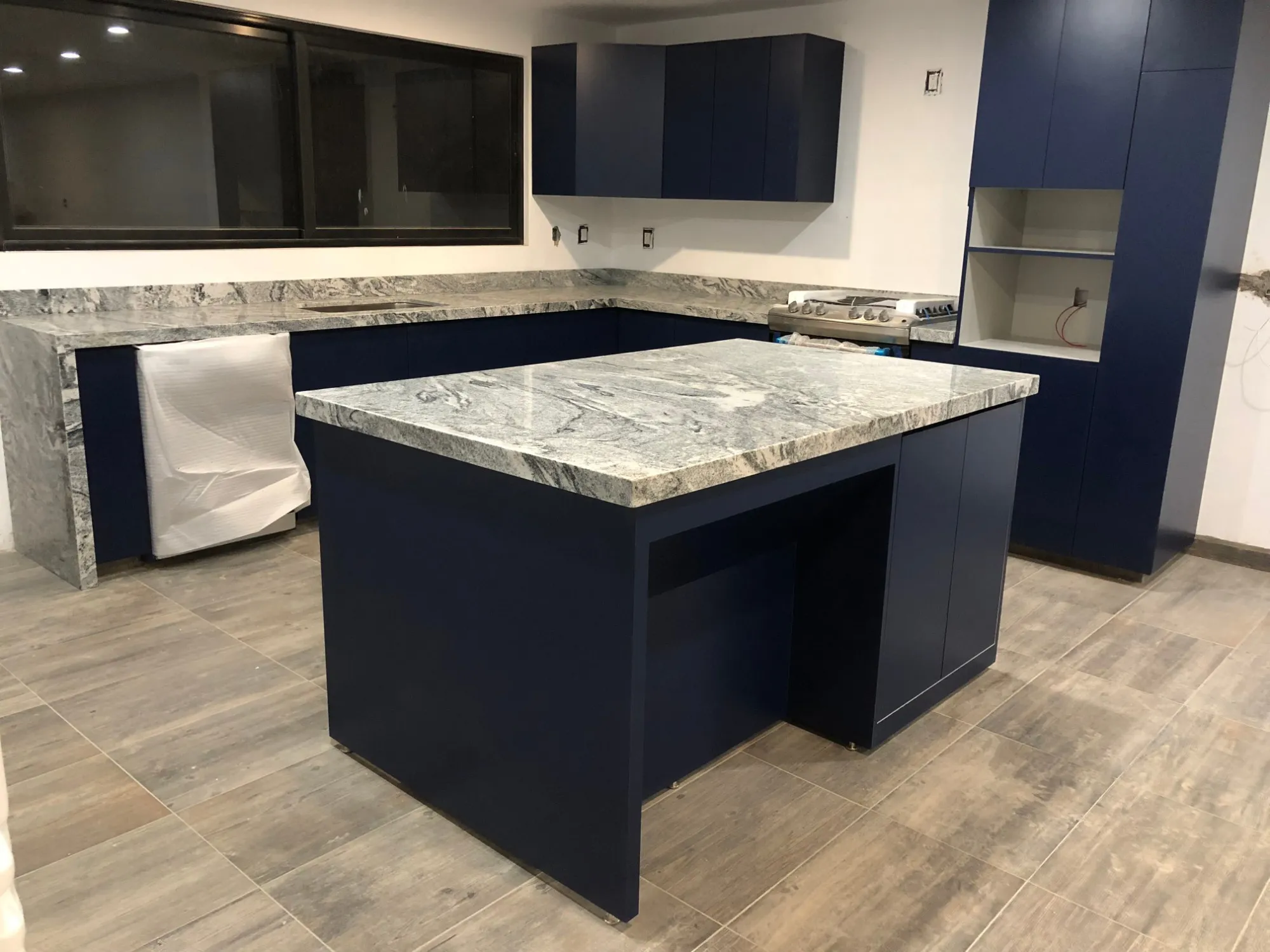 Cocina con gabinetes azul marino y cubierta de granito gris veteado, con isla central