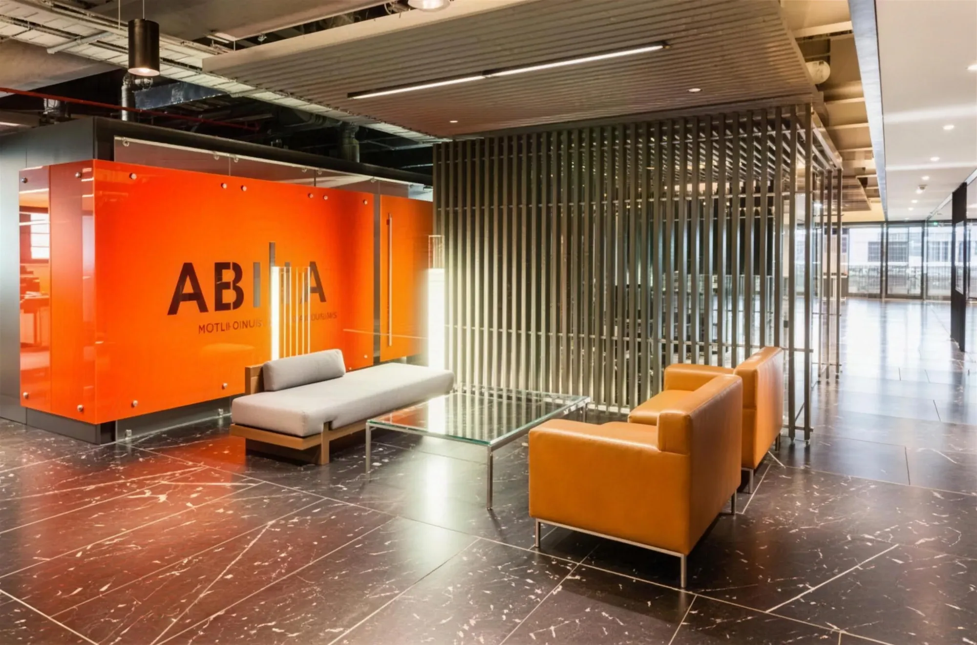 Recepción de oficinas con muro de cristal color naranja, listones metálicos verticales y sala de espera con sillones de piel